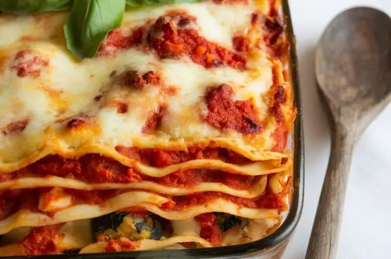 Hearty Vegetarian Lasagne Recipe 11 A hearty vegetarian lasagne with layers of pasta, tomato sauce, vegetables, and melted cheese, garnished with basil on a table.