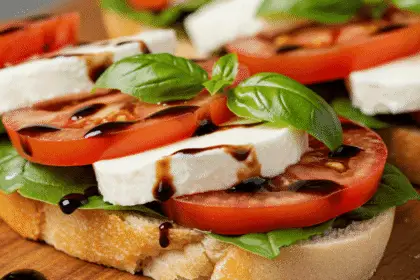 A fresh Caprese sandwich with mozzarella, tomatoes, and basil on a wooden board with balsamic glaze.