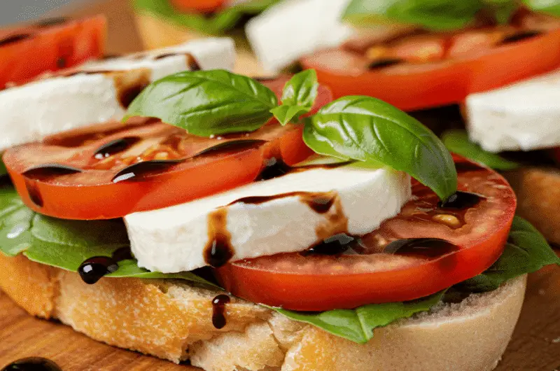 A fresh Caprese sandwich with mozzarella, tomatoes, and basil on a wooden board with balsamic glaze.