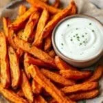 Plate of crispy sweet potato fries with garlic aioli on a rustic wooden table.