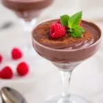 Decadent vegan chocolate avocado mousse in glass dishes garnished with raspberries and cocoa powder.