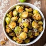 Crispy air fried Brussels sprouts garnished with Parmesan cheese in a rustic bowl on a wooden table.