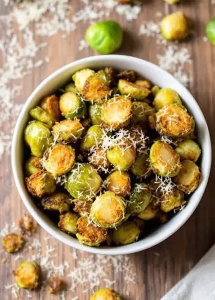 Crispy air fried Brussels sprouts garnished with Parmesan cheese in a rustic bowl on a wooden table.