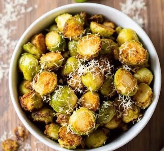 Crispy air fried Brussels sprouts garnished with Parmesan cheese in a rustic bowl on a wooden table.
