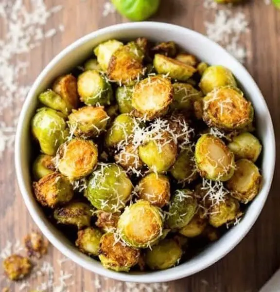 Crispy air fried Brussels sprouts garnished with Parmesan cheese in a rustic bowl on a wooden table.