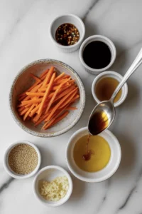 ingredients for Glossy julienned carrot salad coated in a spicy chili garlic oil dressing, garnished with sesame seeds, scallions, and fresh herbs. This vibrant vegan side dish is inspired by the viral TikTok carrot salad trend and features a mix of savory, tangy, and slightly sweet flavors with a juicy, well-dressed texture