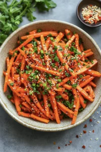 Glossy julienned carrot salad coated in a spicy chili garlic oil dressing, garnished with sesame seeds, scallions, and fresh herbs. This vibrant vegan side dish is inspired by the viral TikTok carrot salad trend and features a mix of savory, tangy, and slightly sweet flavors with a juicy, well-dressed texture