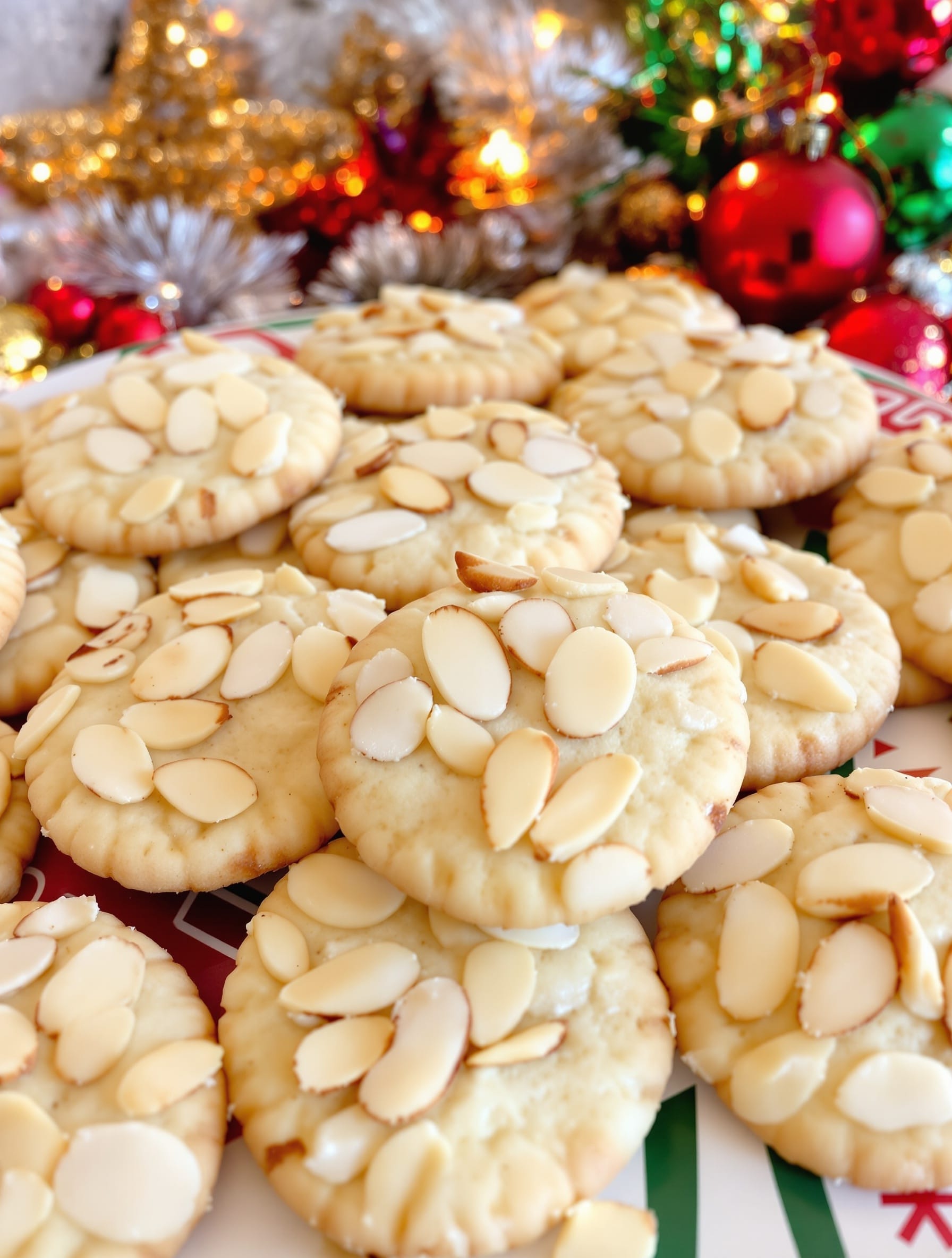 A plate of almond cookies topped with sliced almonds, surrounded by festive decorations.